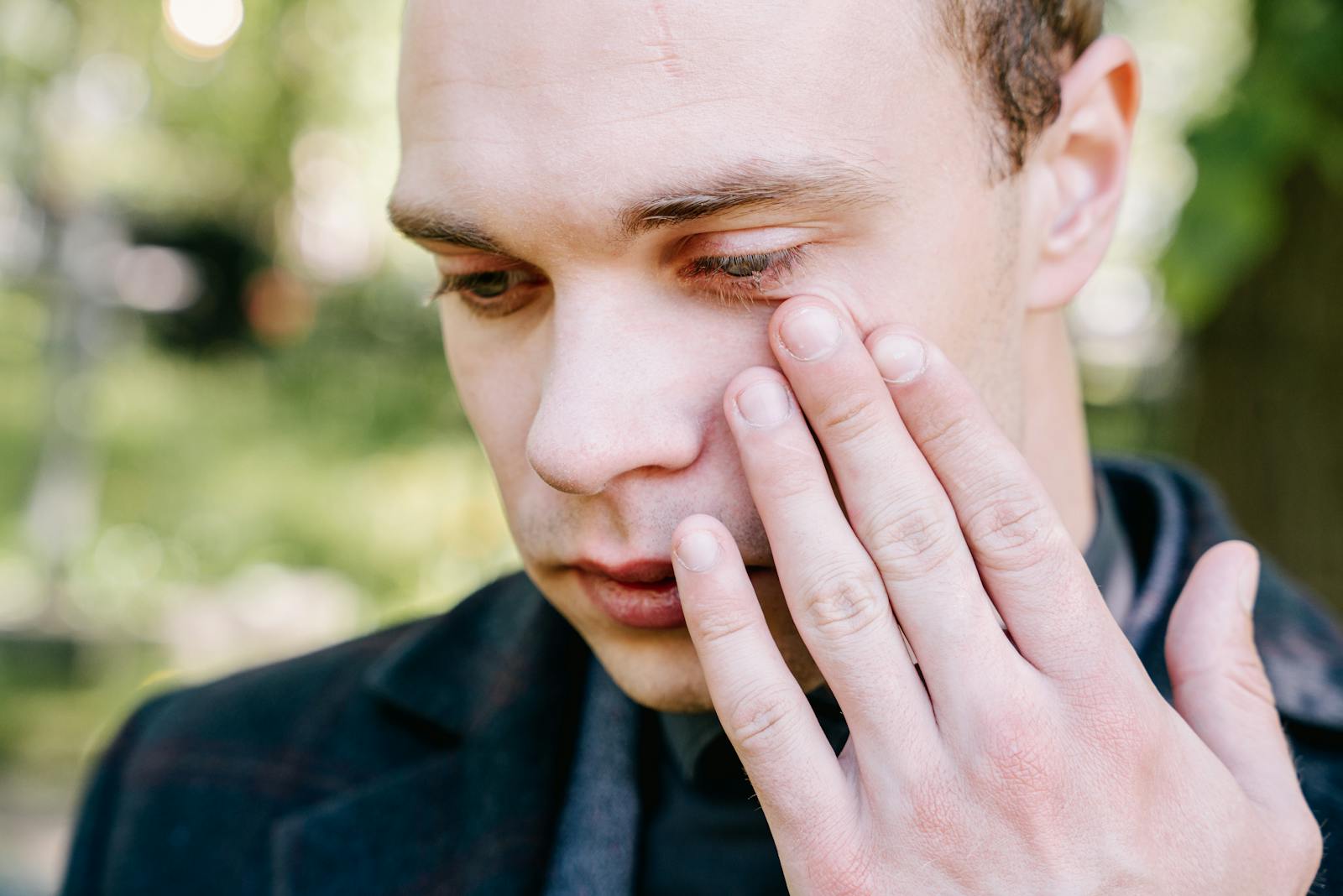 A close-up portrait of a man outdoors, displaying emotions with hand on his face.